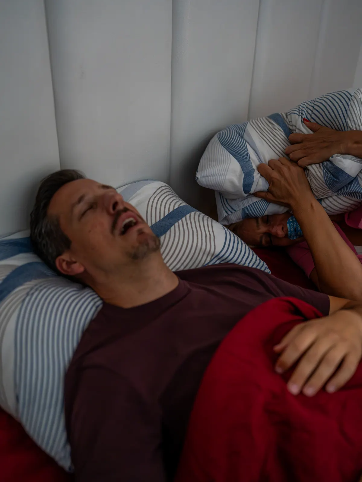 Bračni krevet noću, žena mirno spava okrenuta ka mužu koji leži na leđima sa Noro trakicom na nosu